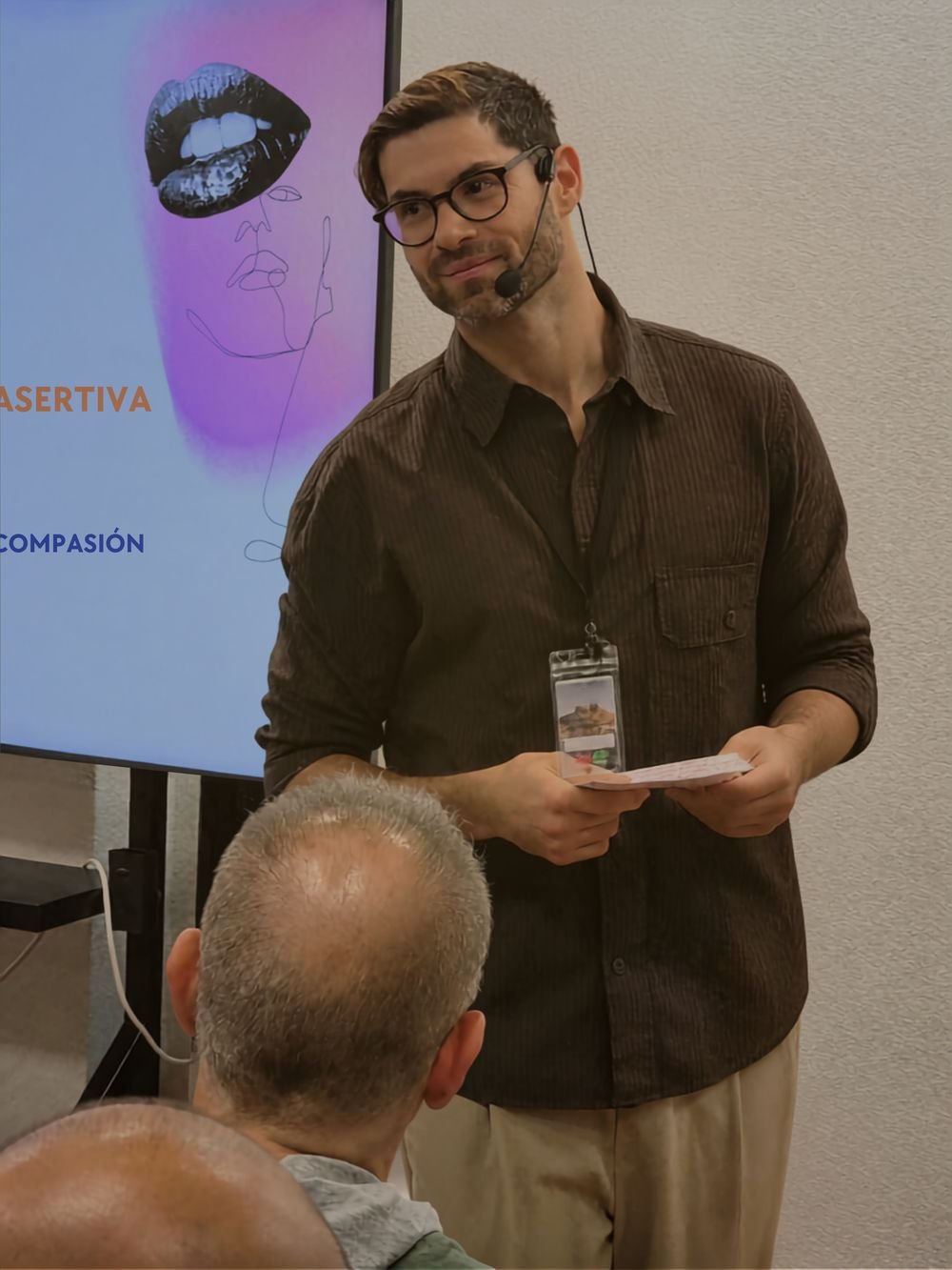 Pau Sanz impartiendo un taller en Orlander con micrófono de diadema, ante una pantalla sobre comunicación asertiva y compasión